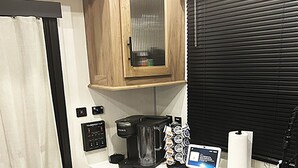 A compact kitchenette with a coffee maker, a small refrigerator, a cutting board, and a window with blinds. - Cover RV Pad w/Large 45ft Destination RV & Outdoor Bar / Hot Tub (Bolivar Peninsula)