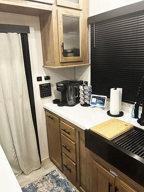 A compact kitchenette with a coffee maker, a small refrigerator, a cutting board, and a window with blinds. - Cover RV Pad w/Large 45ft Destination RV & Outdoor Bar / Hot Tub (Bolivar Peninsula)