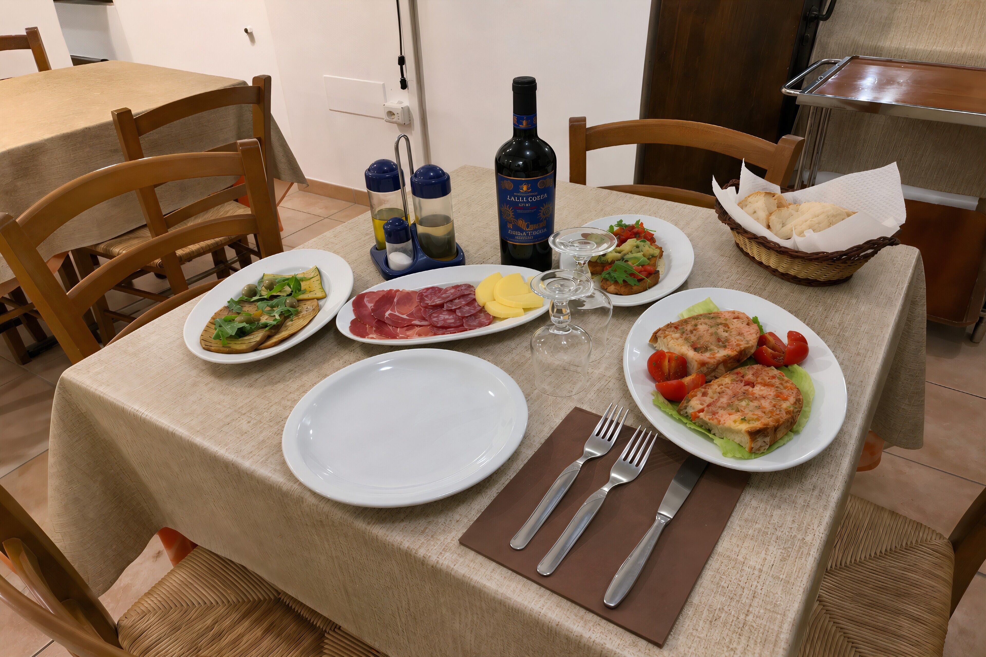 A dining table with plates of food, a bottle of wine, salt and pepper shakers, and a basket of bread.