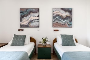 A double room with two beds, a small bedside table with a plant, and abstract wall art. - Nikiforos Apartments (Corfu)