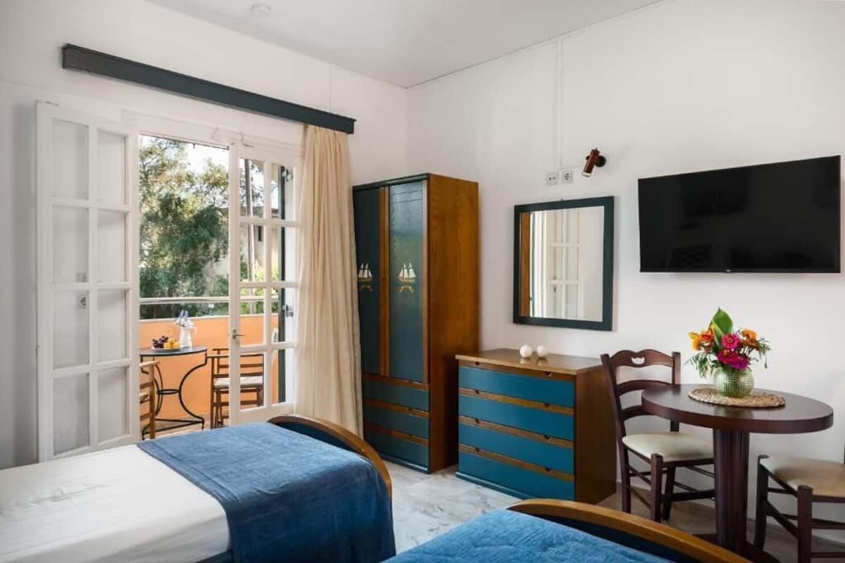 Un dormitorio con dos camas, un armario, un televisor y un balcón con mesa y sillas.