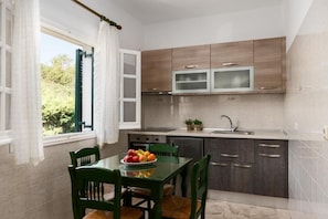 A compact kitchen with wooden cabinets, a built-in microwave, and a dining area with a table and chairs. - Nikiforos Apartments (Corfu)