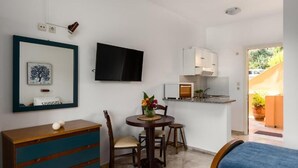 A compact room with a bed, a small dining table with chairs, a TV mounted on the wall, a kitchenette, and a door leading outside. - Nikiforos Apartments (Corfu)