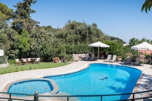 A swimming pool with a curved edge, surrounded by lounge chairs and umbrellas, set against a backdrop of trees and a clear sky. - Nikiforos Apartments (Corfu)