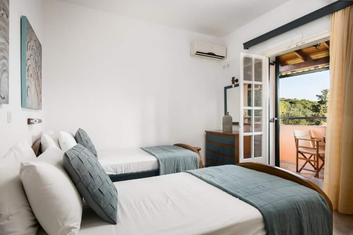Un dormitorio con dos camas, un armario, un equipo de aire acondicionado y un balcón con una mesa y sillas.