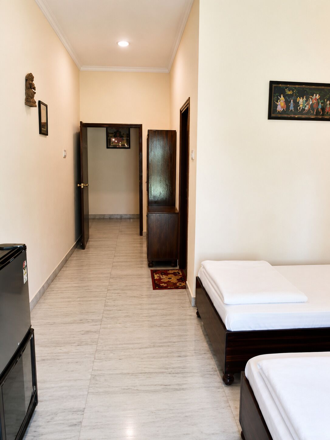 A hotel corridor with a bed on the right, a wardrobe, and a door leading to another room.