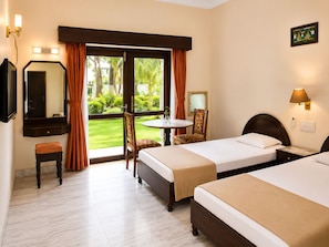 Habitación de hotel con dos camas, una mesita, una silla, un espejo y una ventana con cortinas.