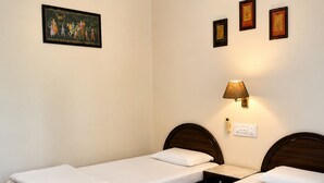 A hotel room with two single beds, a nightstand, a wall-mounted lamp, and a painting.