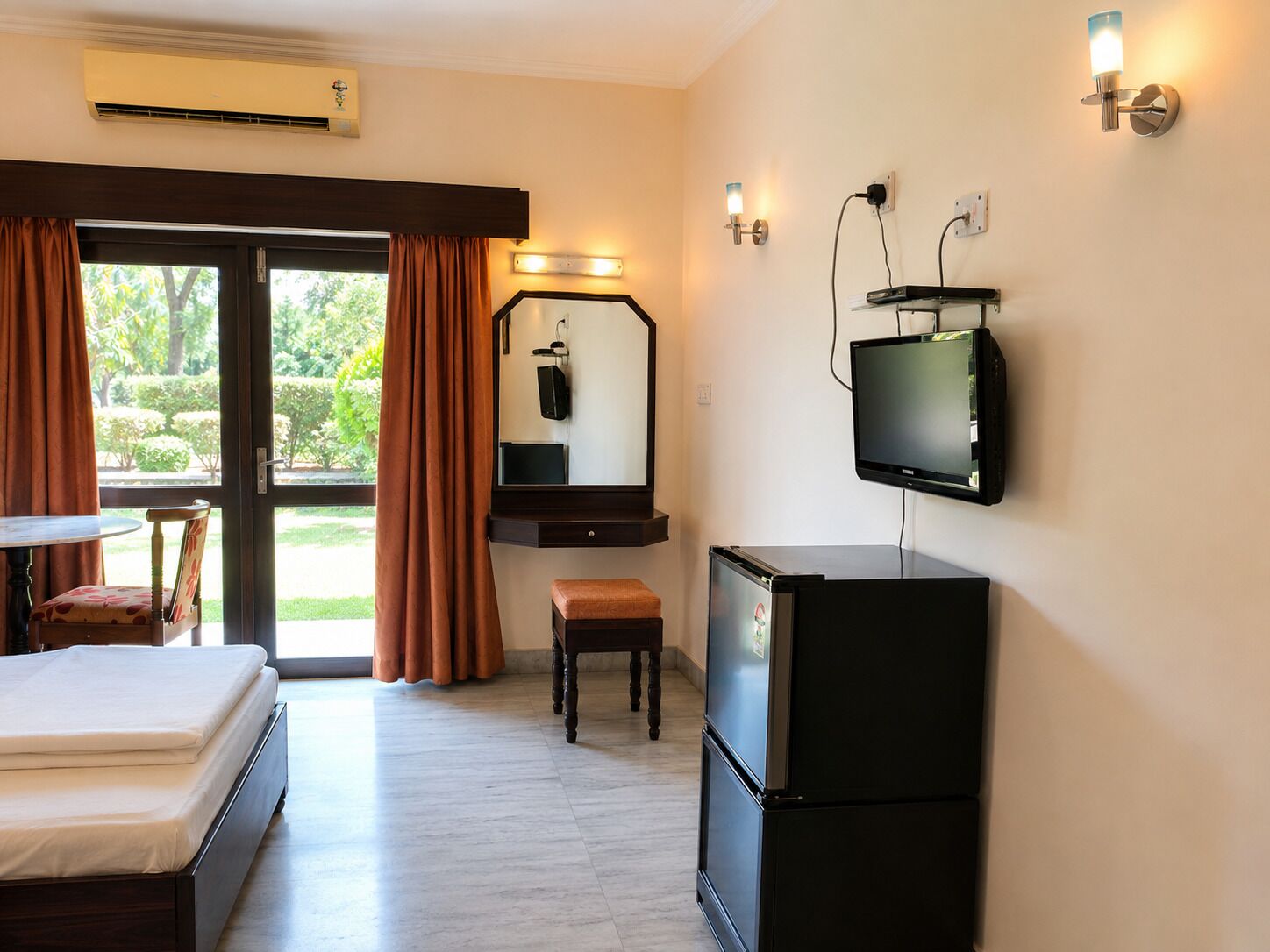 A hotel room with a bed, a desk, a television, and a small refrigerator.