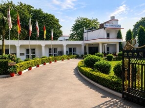 A hotel entrance with a curved driveway, a gated entrance, and multiple flags. - Hotel Ganesha  (Khajuraho)