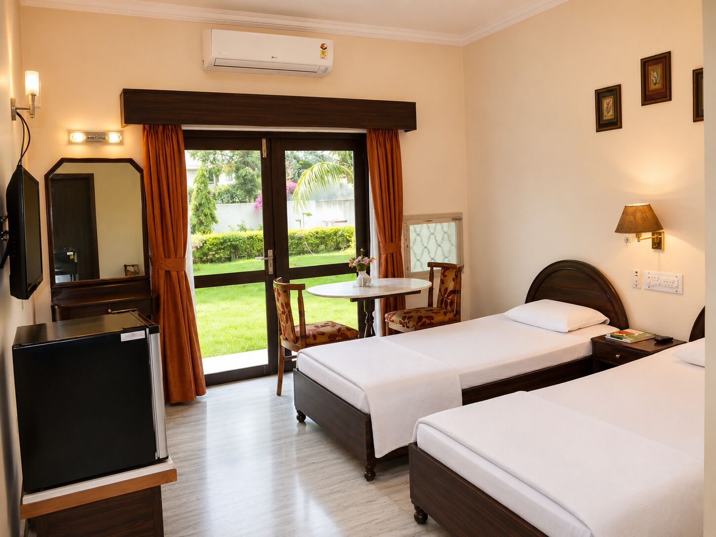 A hotel room with two beds, a desk, a television, a window with curtains, and an air conditioning unit.