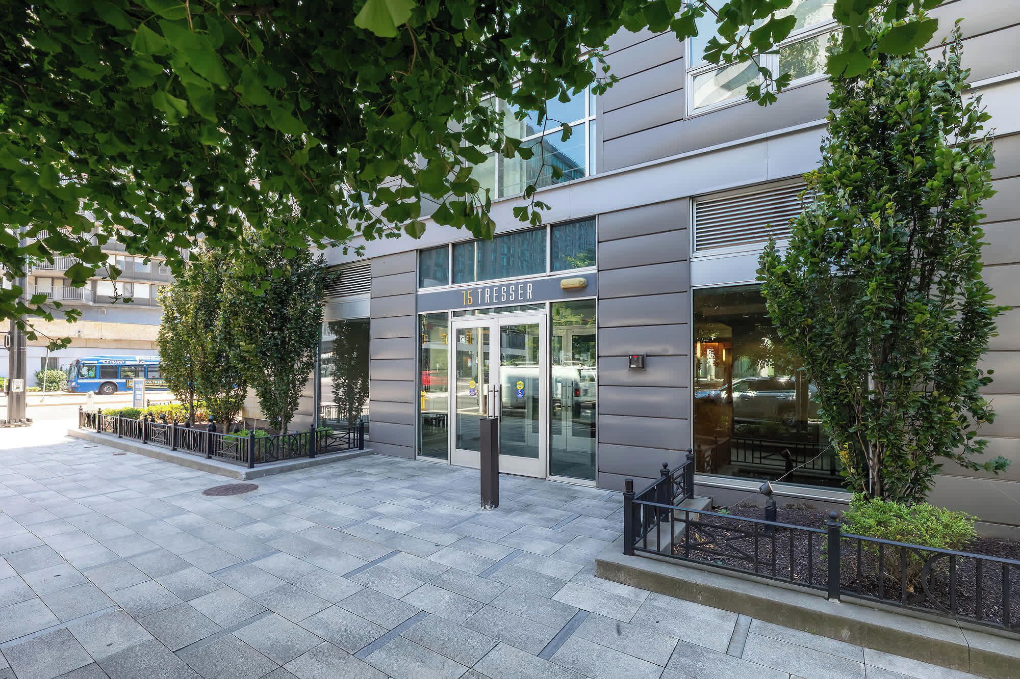 A modern building with a glass entrance, a metal fence, and a tree in front.