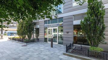 A modern building with a glass entrance, a metal fence, and a tree in front.