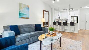 A modern living room with a grey sofa, a glass coffee table, and a painting on the wall.