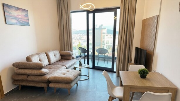 A modern living room with a sofa, a dining table with chairs, a small table with a plant, and a large sliding glass door leading to a balcony. - Sunny Stay apartment in Ksamil (Ksamil)