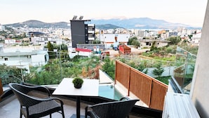 A balcony with two wicker chairs, a small table with a potted plant, and a view of a cityscape with buildings and mountains in the background. - Sunny Stay apartment in Ksamil (Ksamil)