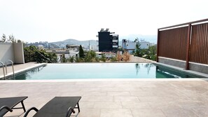 Ein Pool im Freien mit Liegestühlen, Blick auf die Stadt und ein modernes Gebäude im Hintergrund.