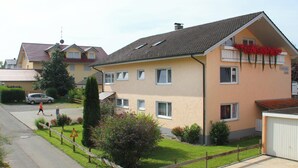 A residential building with a sloped roof, multiple windows, and a small garden area with a fence. - Studio Apartment Braun (Wasserburg am Bodensee)