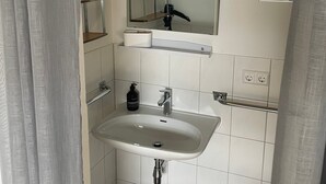A bathroom with a white sink, a mirror, a towel rack, and a shower curtain. - Studio Apartment Braun (Wasserburg am Bodensee)