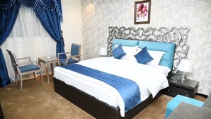 A hotel room with a large bed, a desk, a chair, and a nightstand. - Diva Serviced Apartments (Jeddah)