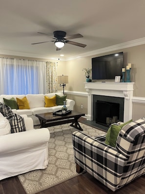 A living room with a white sofa, plaid armchair, fireplace, television, and a ceiling fan. - Beautiful 3 bed/2 bath with Private Suite (Lillington)