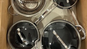 Un cajón con cuatro ollas de acero inoxidable y sus tapas, un colador y un asa.
