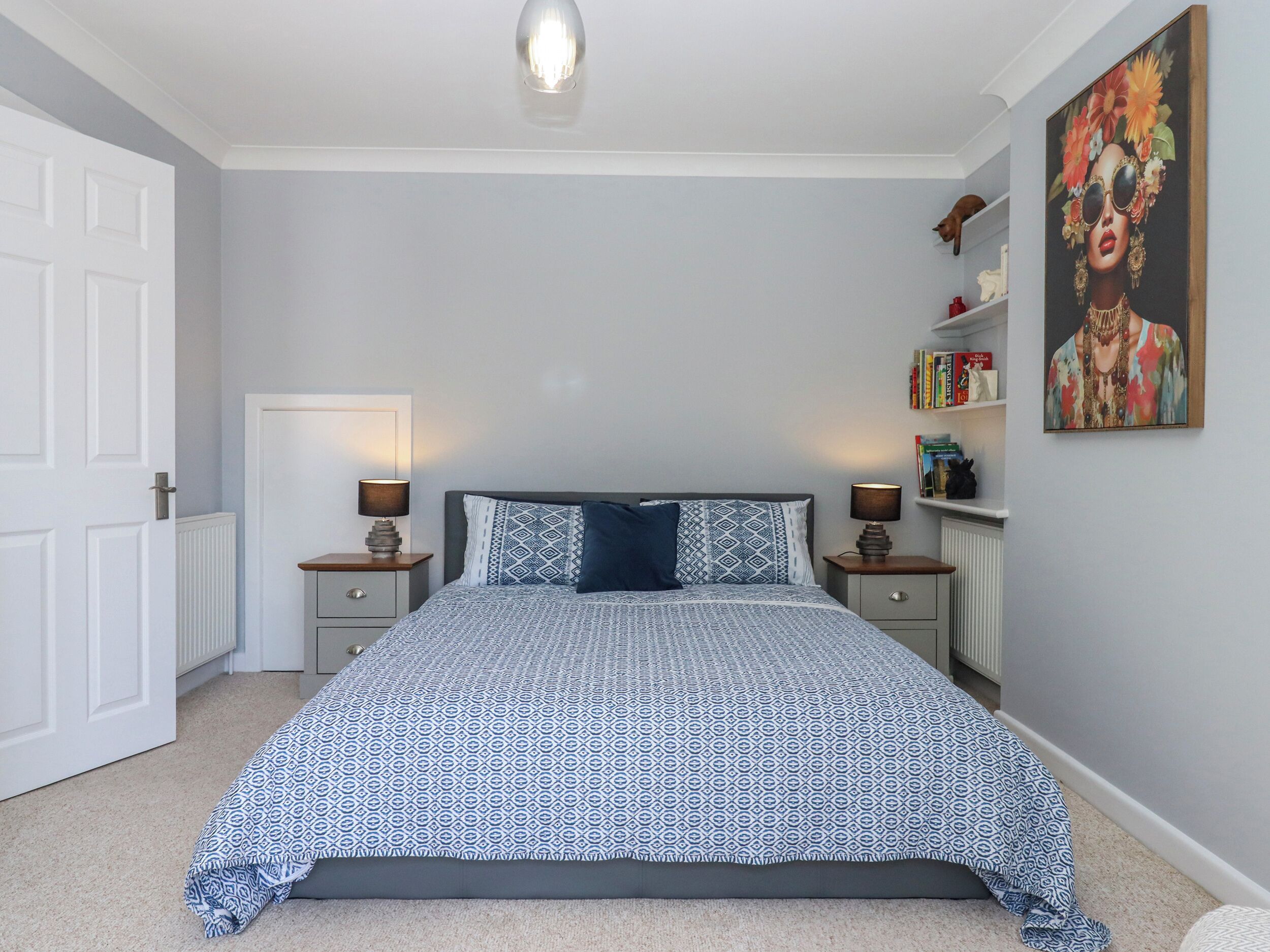 Un dormitorio con cama, mesitas de noche, un radiador, una puerta y una estantería.