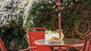 Juego de mesa y sillas metálicas rojas al aire libre, con una jarra de vidrio, un bol de croissants y un vaso de limonada.