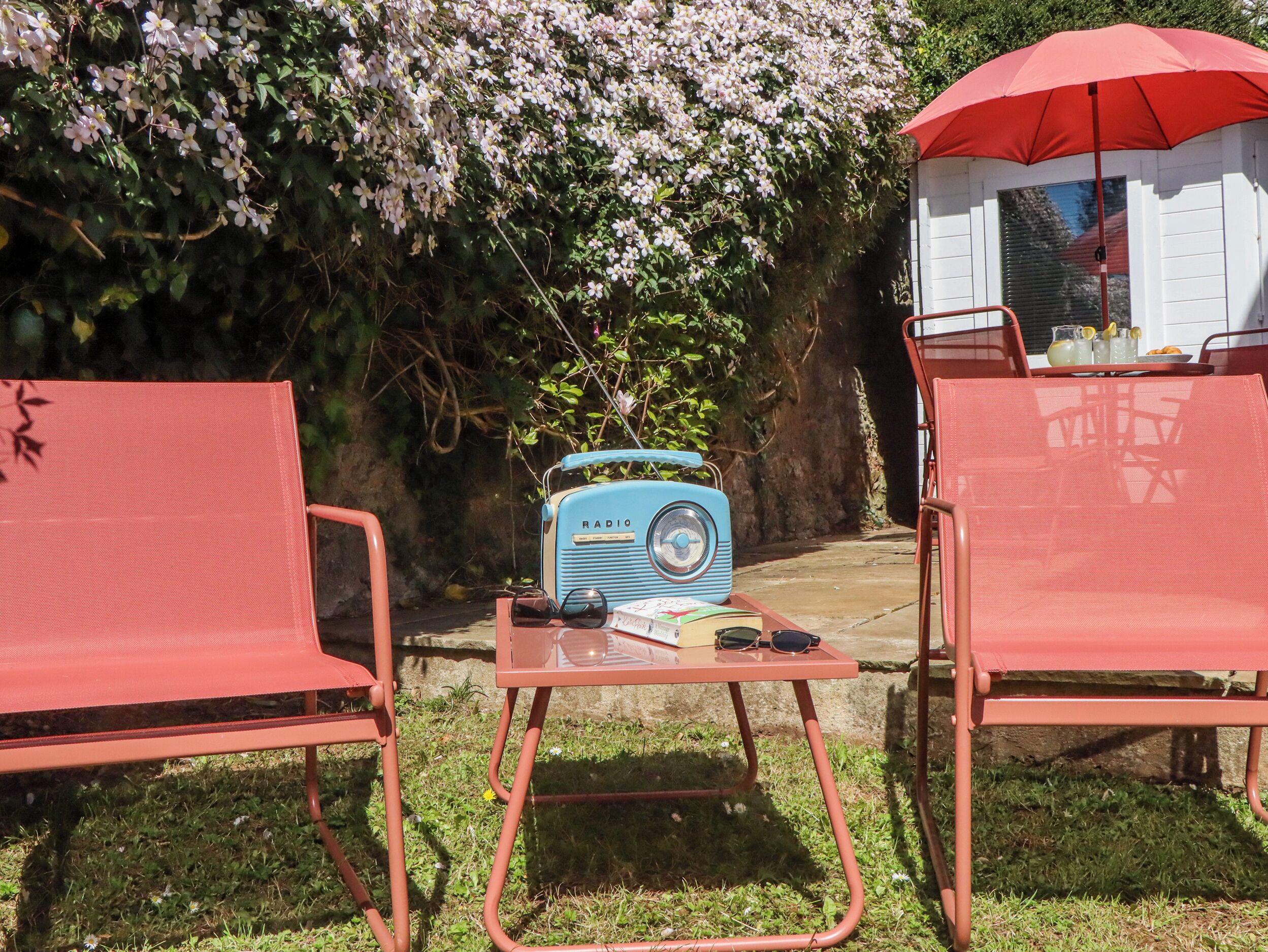 A garden with two red chairs, a vintage blue radio, and a red umbrella.