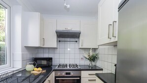 Une cuisine compacte avec des meubles blancs, un plan de travail noir, un four à micro-ondes, un four traditionnel et un réfrigérateur en acier inoxydable.