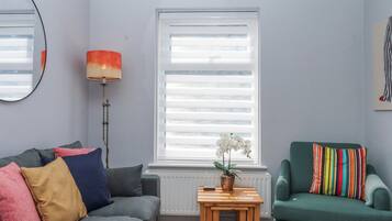 A living room with a grey sofa, a green armchair, a small wooden table with a plant, and a radiator.
