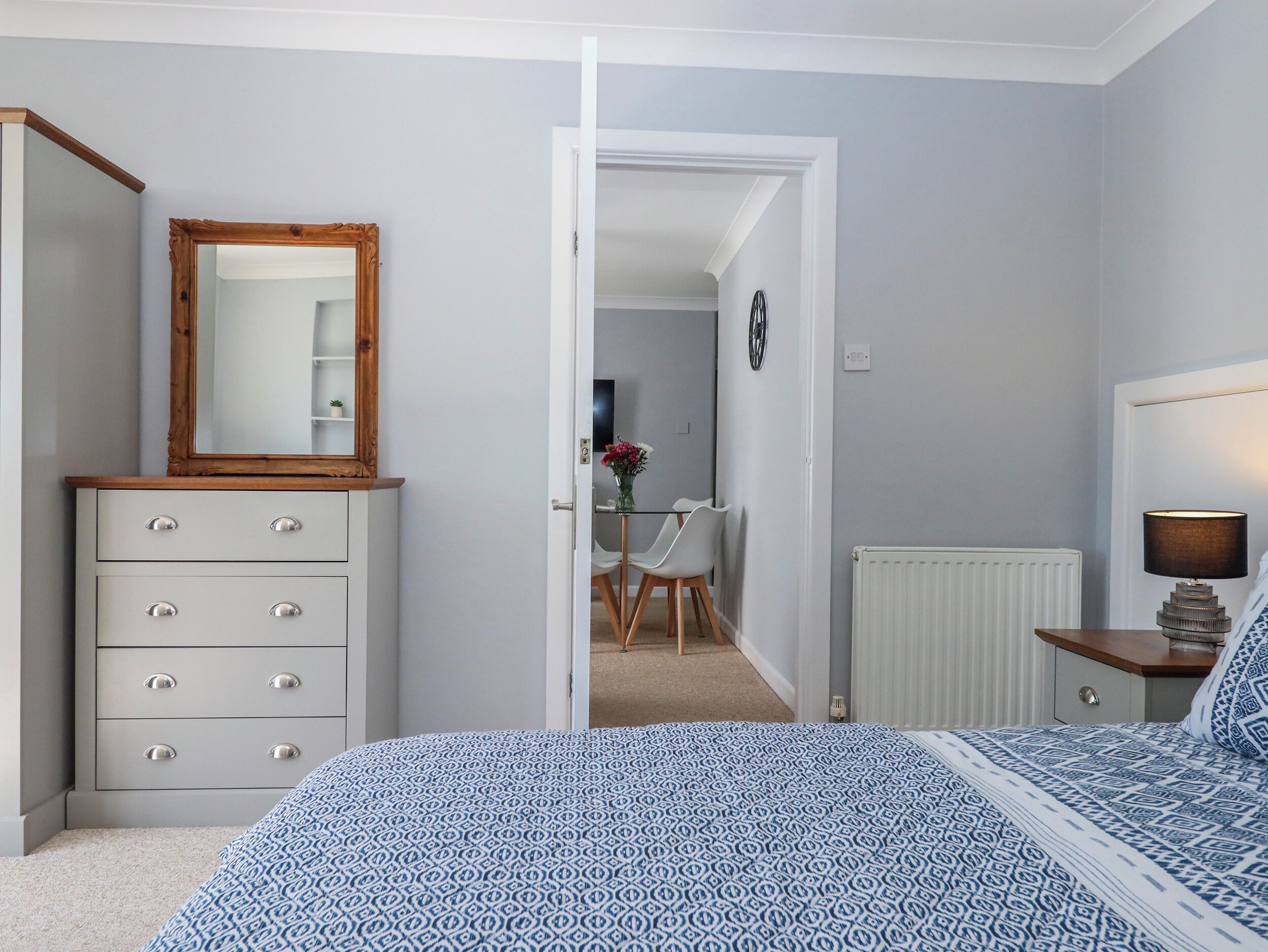 A bedroom with a bed, dresser, mirror, and a door leading to another room.