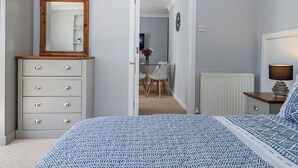 Une chambre à coucher comprenant un lit, une commode, un miroir et une porte donnant sur une autre pièce.