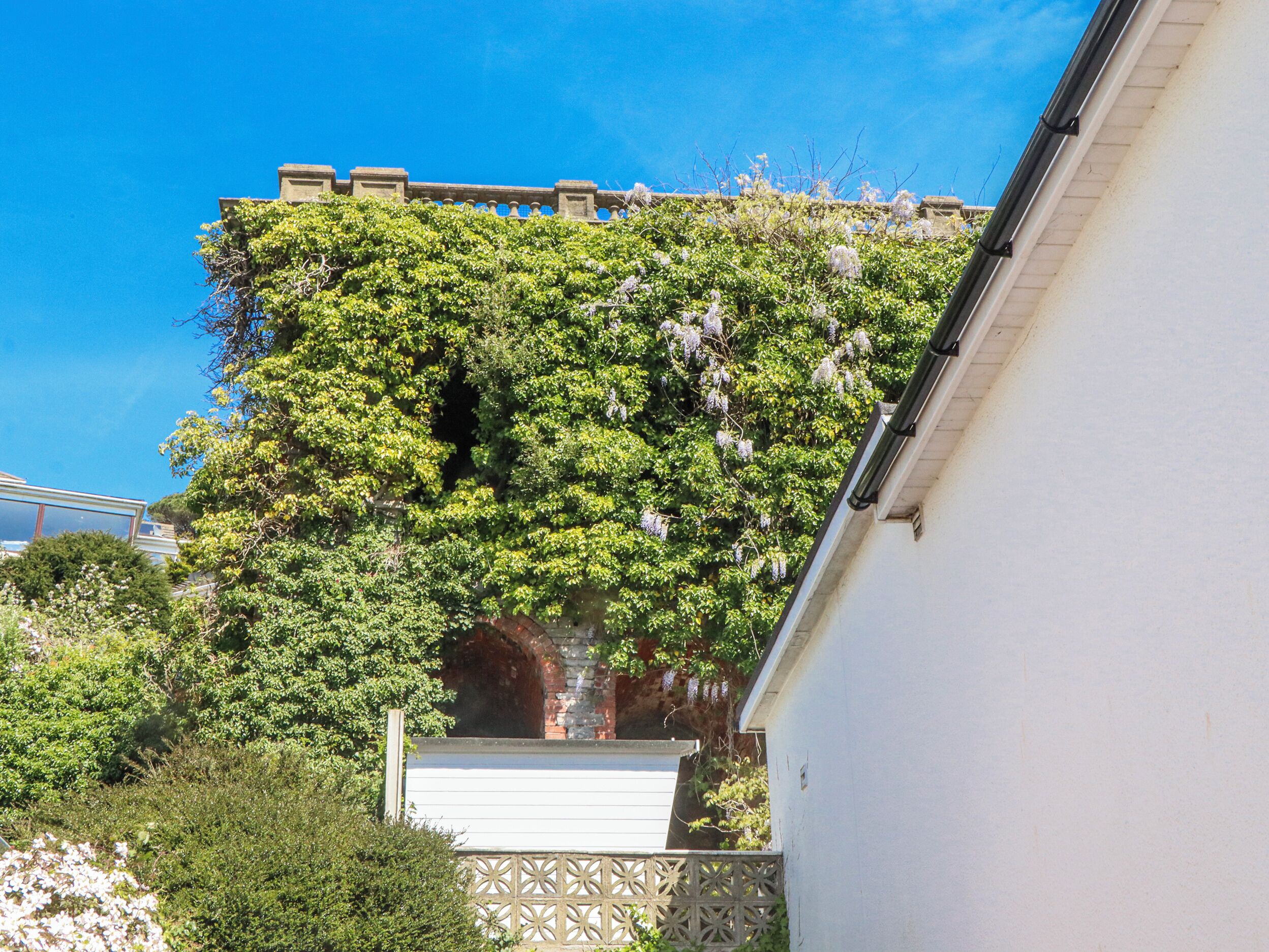 Ein Gebäude mit weißer Fassade, einem sichtbaren Fenster und einer dahinterliegenden Backsteinmauer.