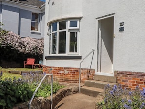 A house with a white exterior, a brick base, a red door, and a window with a white frame. - The Arches (Torquay)