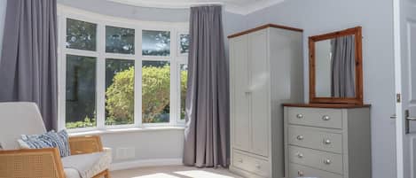 A bedroom with a large window, a wardrobe, a bed, and a rocking chair.