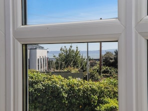 A view through a window with a white frame, a hedge in the foreground, and a body of water with buildings in the background. - The Arches (Torquay)