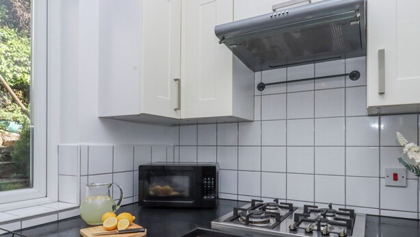 A kitchen with white cabinets, a black countertop, a microwave, a gas stove, and a window with greenery outside. - The Arches (Torquay)