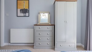 A bedroom with a grey wardrobe, a bedside table with a mirror, a radiator, and a framed picture on the wall. - The Arches (Torquay)