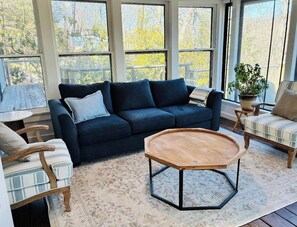 A cozy room with a dark blue sofa, a wooden coffee table, and a view of trees through large windows.