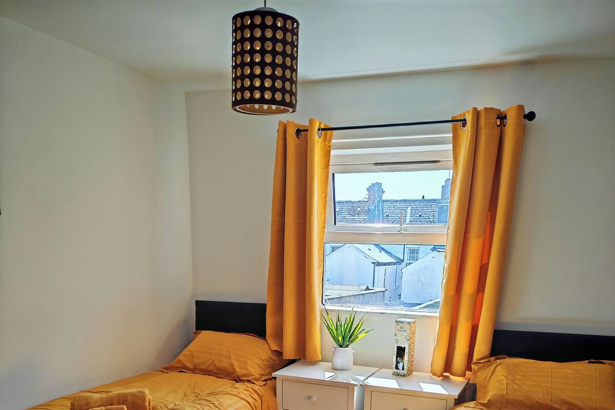 A hotel room with two beds, a desk, a potted plant, and a window with curtains.