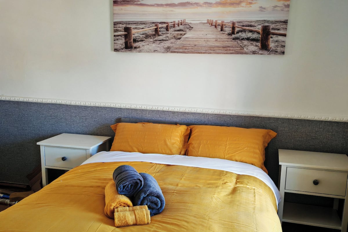 A hotel room with a bed, a nightstand, a drawer, a painting on the wall, and a blue towel on the bed.
