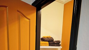 A bathroom with a toilet, a shelf with towels, and a door with a wooden frame.