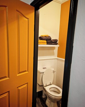 Un baño con inodoro, repisas con toallas y una puerta de madera.
