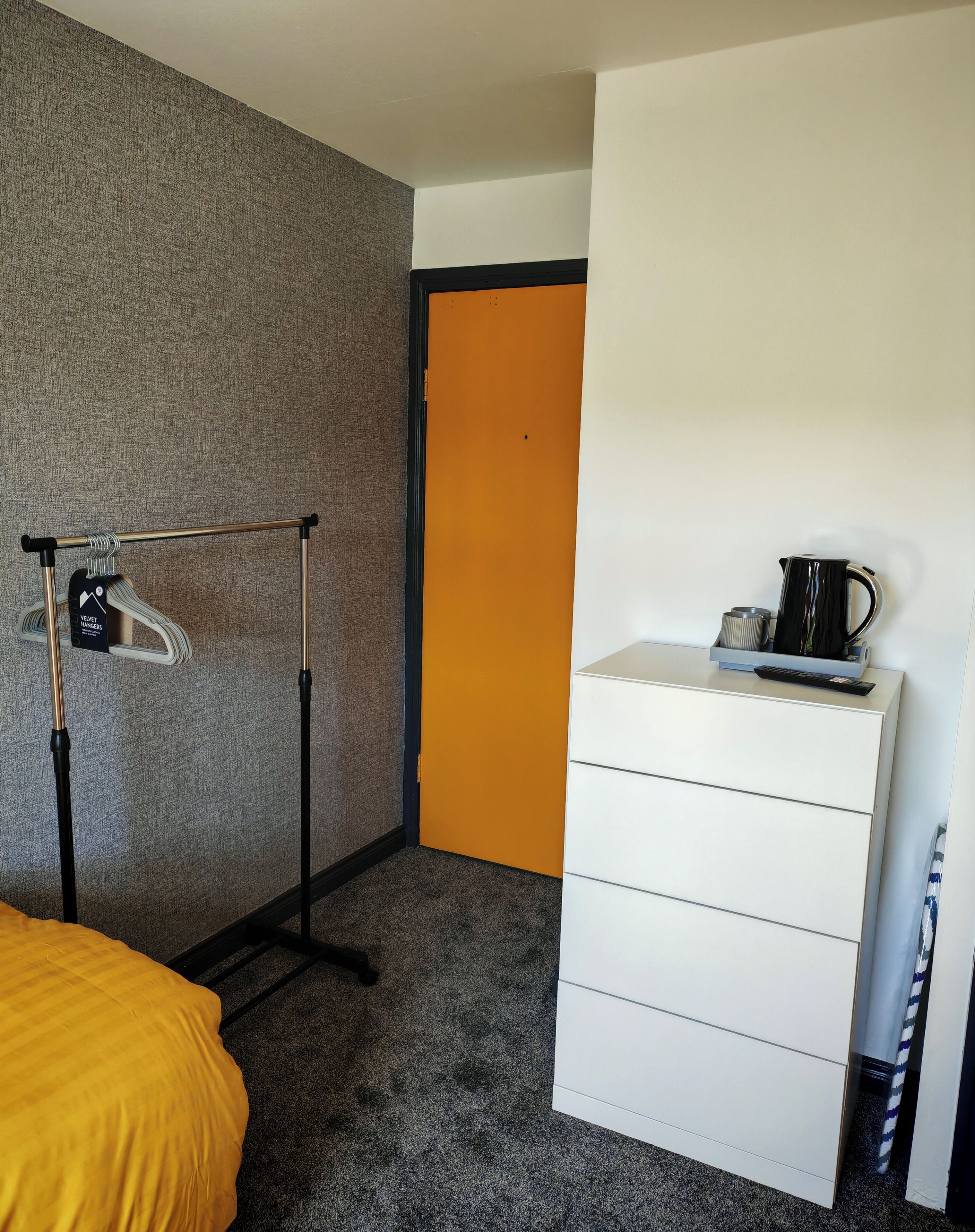 A hotel room with a bed, a wardrobe, a coat rack, and a coffee maker.