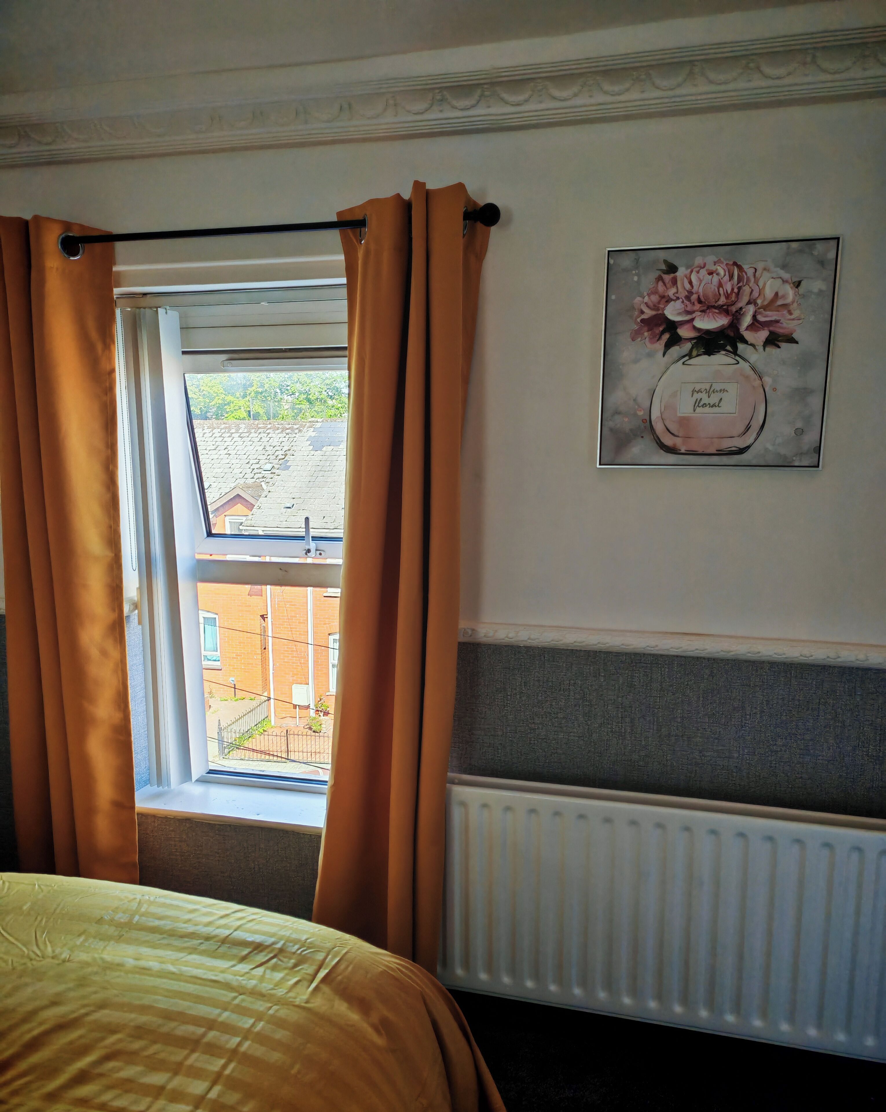 Una habitación con una cama, un radiador, una ventana con cortinas y un cuadro en la pared.
