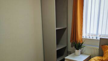 A bedroom with a bed, a nightstand, a wardrobe, a radiator, and a window with curtains.