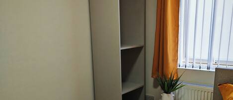 A bedroom with a bed, a nightstand, a wardrobe, a radiator, and a window with curtains.