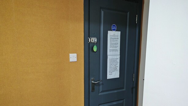 A closed door with a sign, a light switch, and a doorbell on a textured wall.