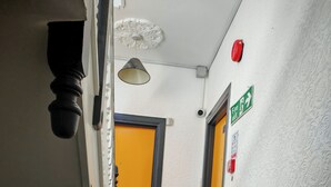 A hallway with a carpeted floor, a black railing, a yellow door, and a fire exit sign.